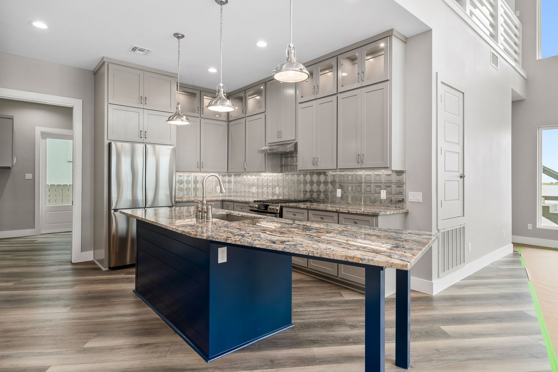 Modern kitchen with gray cabinets, stainless steel appliances, and a blue island with granite countertop.