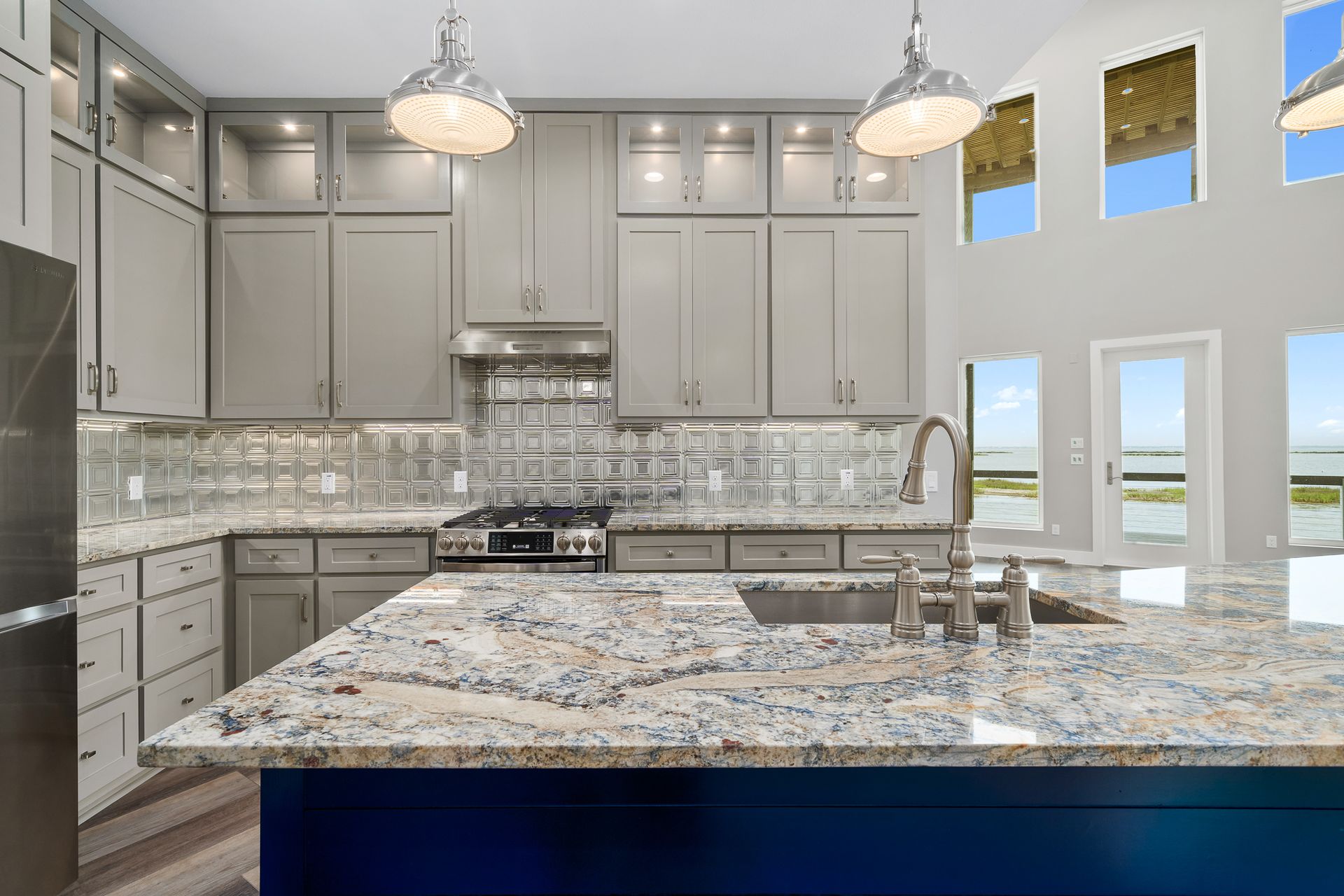 Kitchen with gray cabinets, granite countertops, blue island, and large windows.