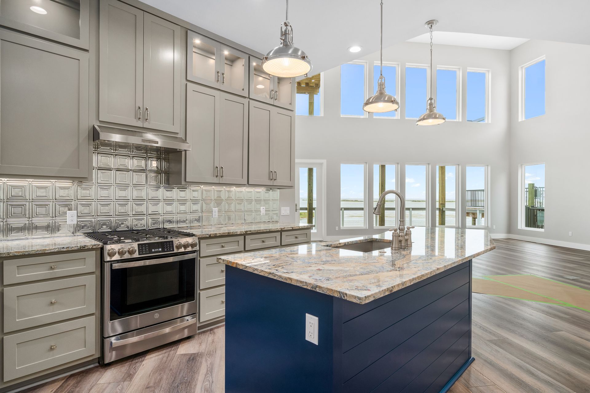 Modern kitchen with blue island, gray cabinets, stainless appliances, and large windows overlooking water.