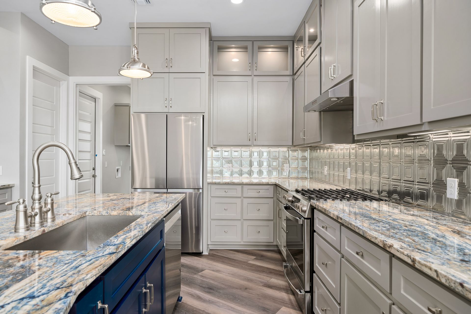 Gray and blue kitchen with a blue island, stainless steel appliances, and decorative backsplash.