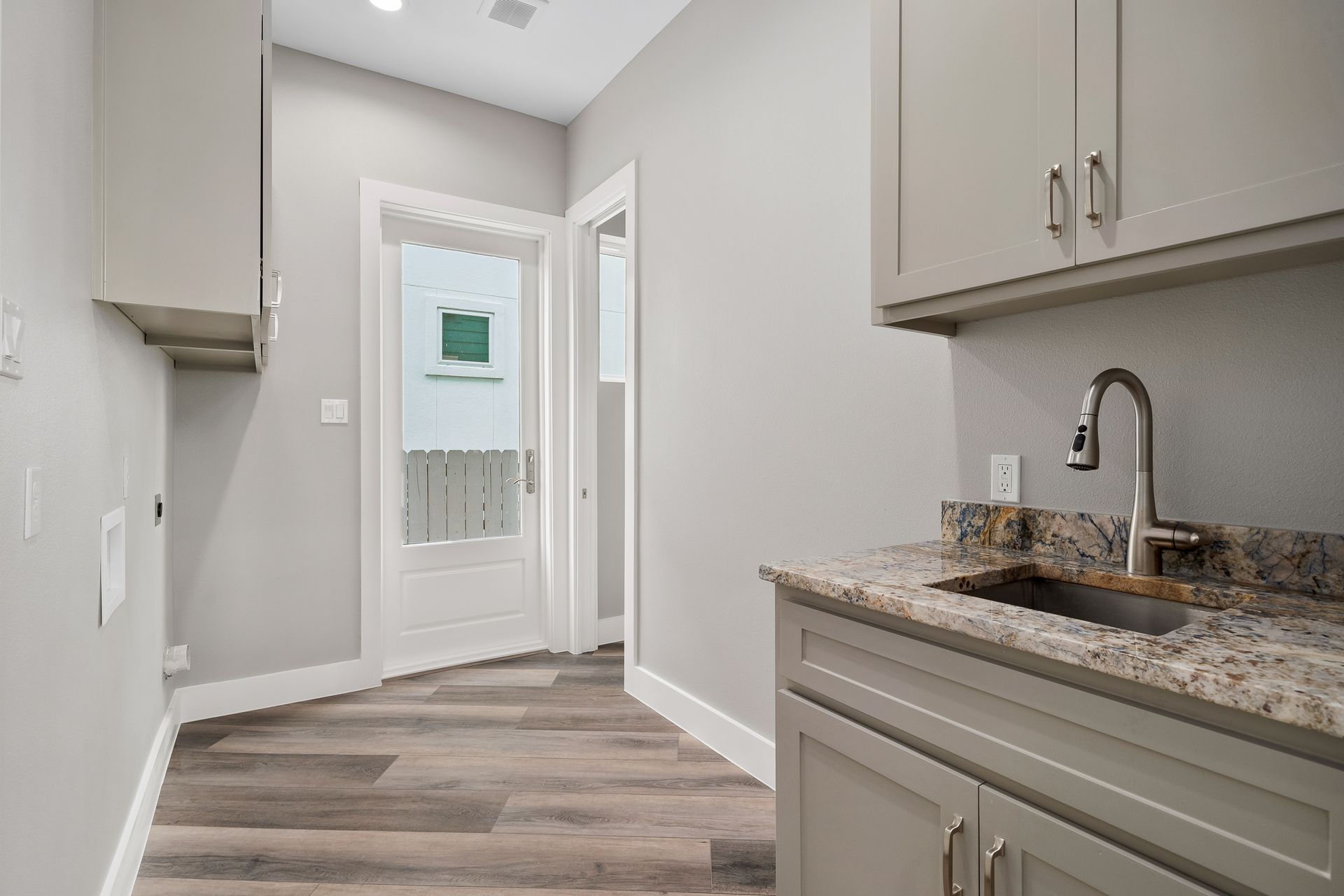 Laundry room with gray cabinets, granite countertop, sink, and door to the outside.