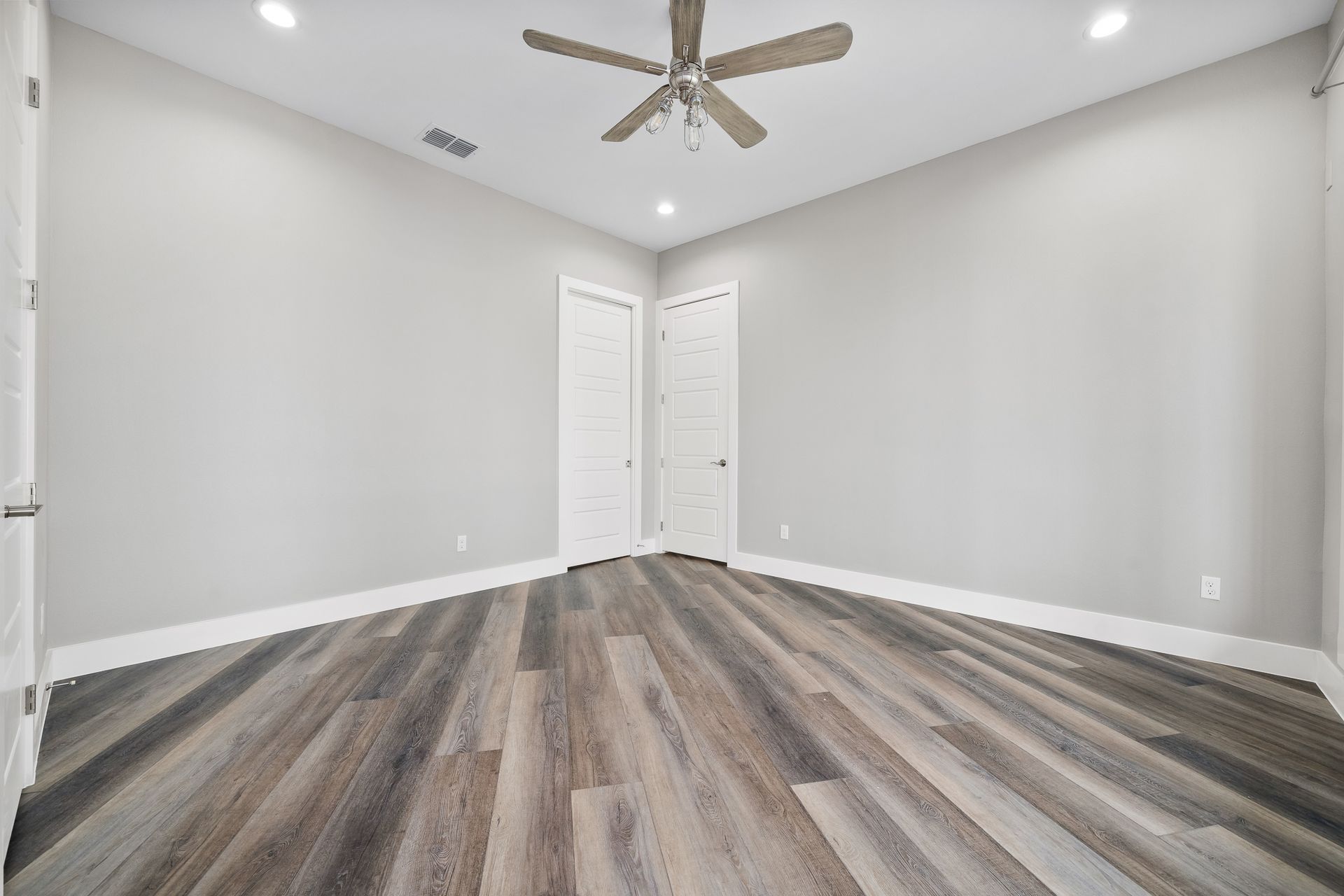 Empty bedroom with gray walls, wood-look floor, white doors, and ceiling fan.