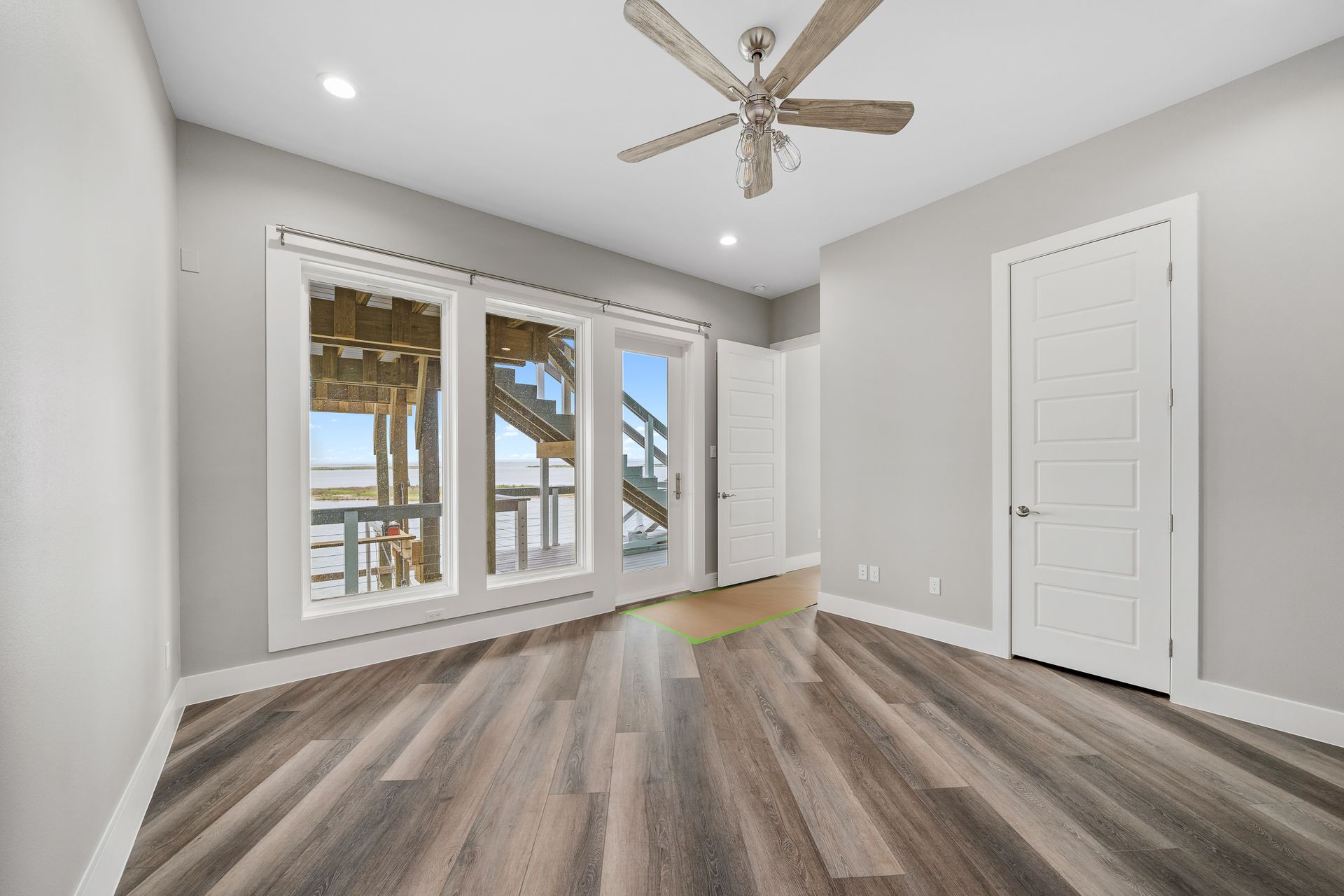 Empty bedroom with hardwood floor, large windows, and light gray walls.