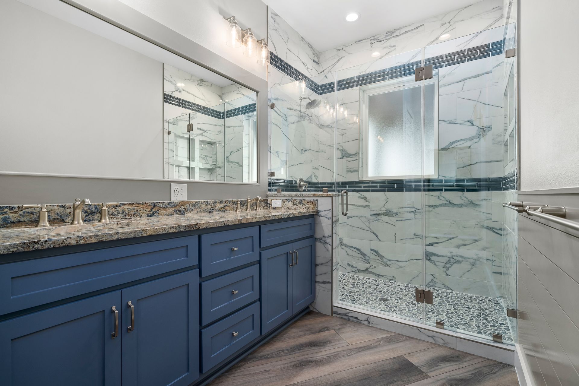 Blue vanity in a modern bathroom with marble-look shower and gray countertop.