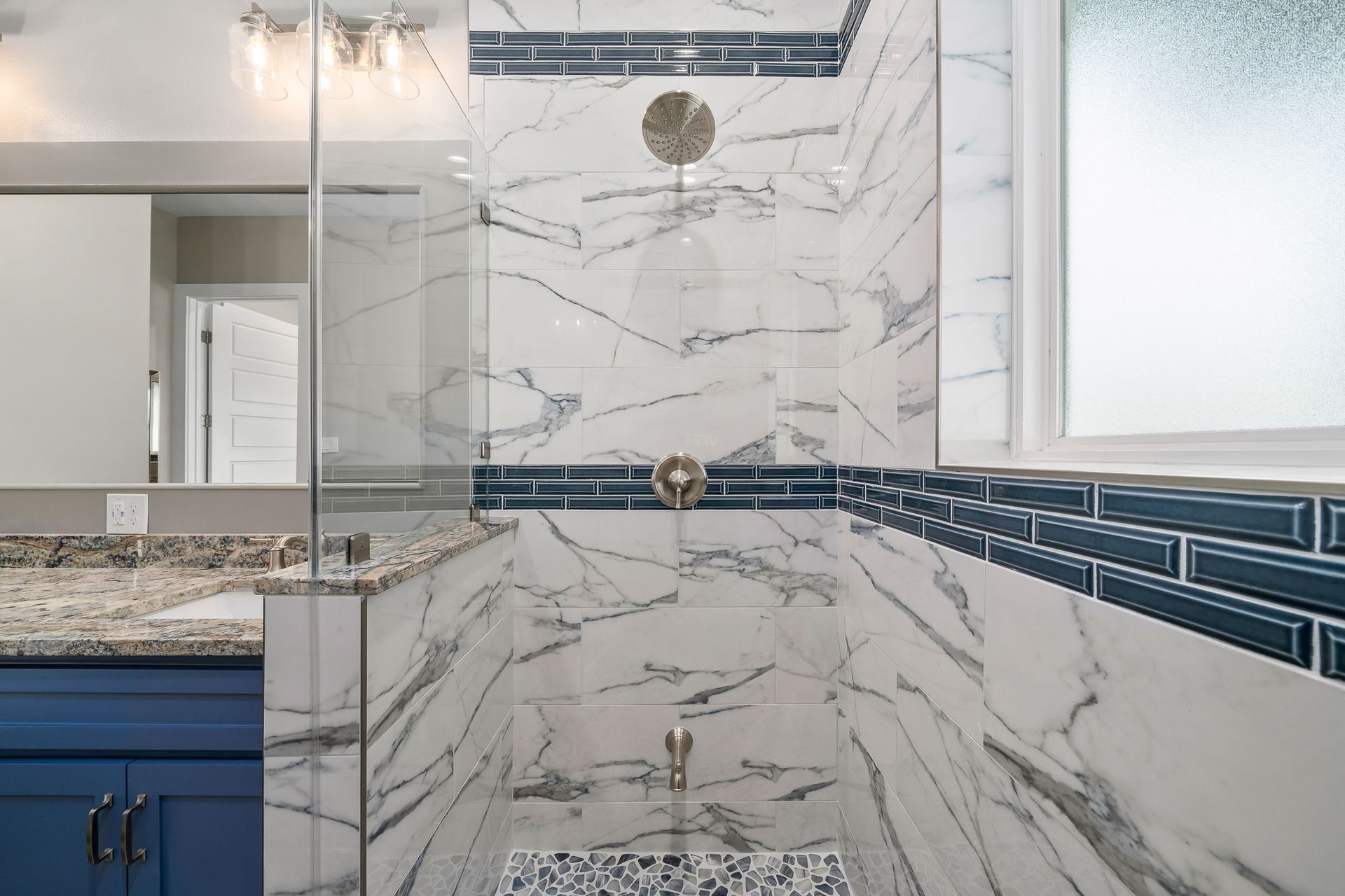 Shower with marble and blue tile, glass door, chrome fixtures, and a window.
