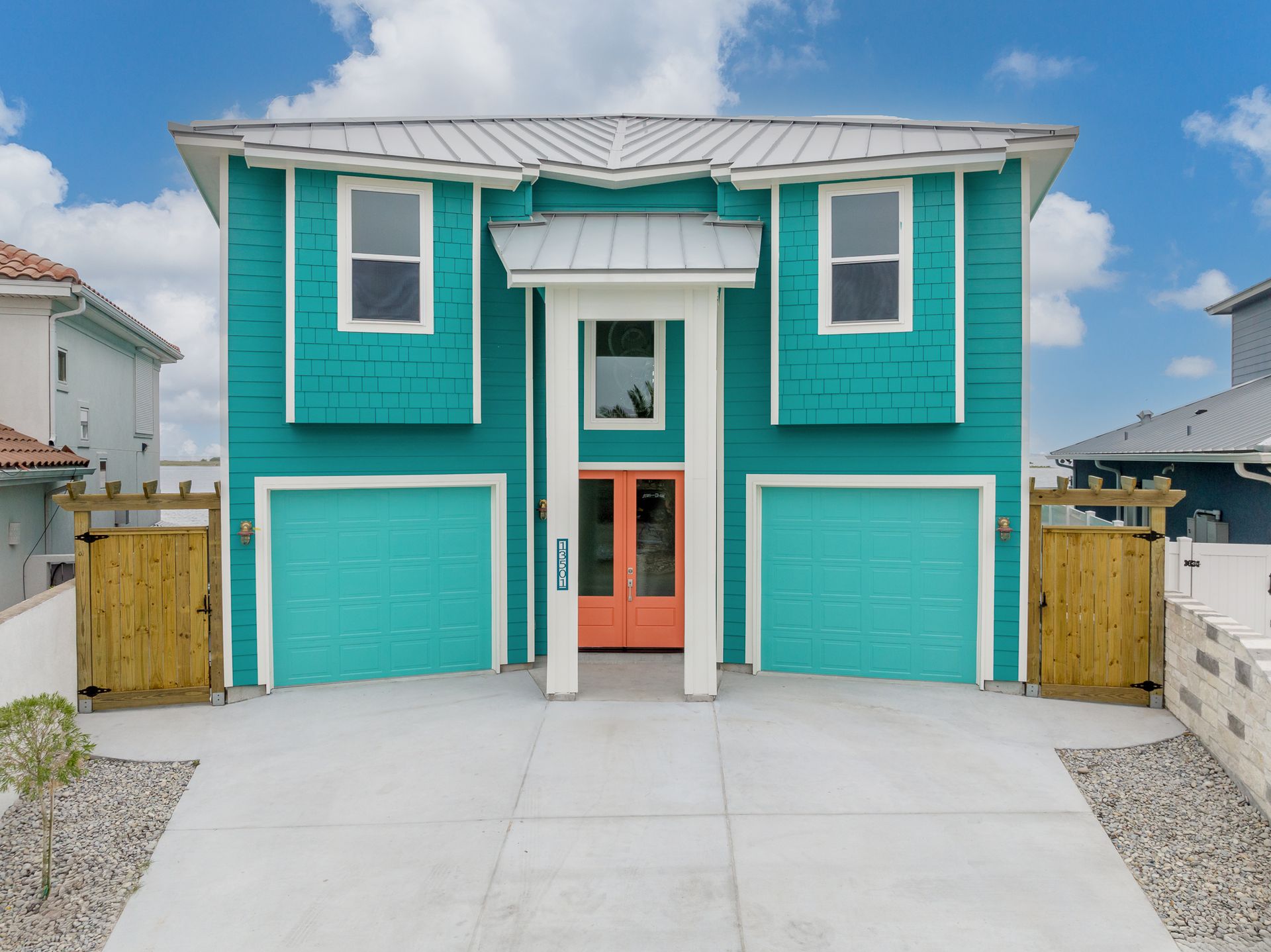 Teal beach house with matching garage doors and peach front door; bright exterior.