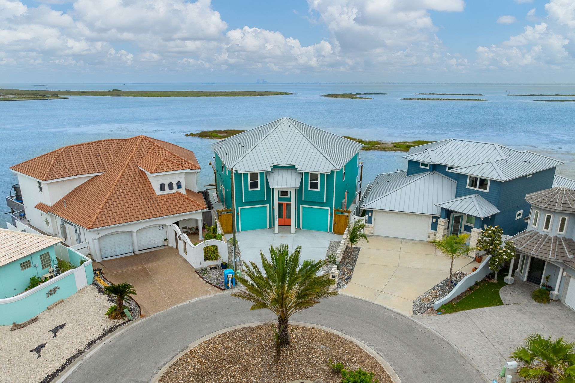 Aerial view of colorful waterfront homes on a coastal inlet with a central palm tree.