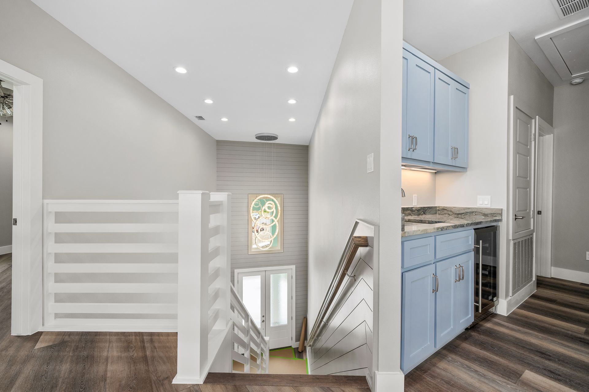 Hallway with stairs, white railing, blue cabinets with a wine fridge, and a neutral color scheme.