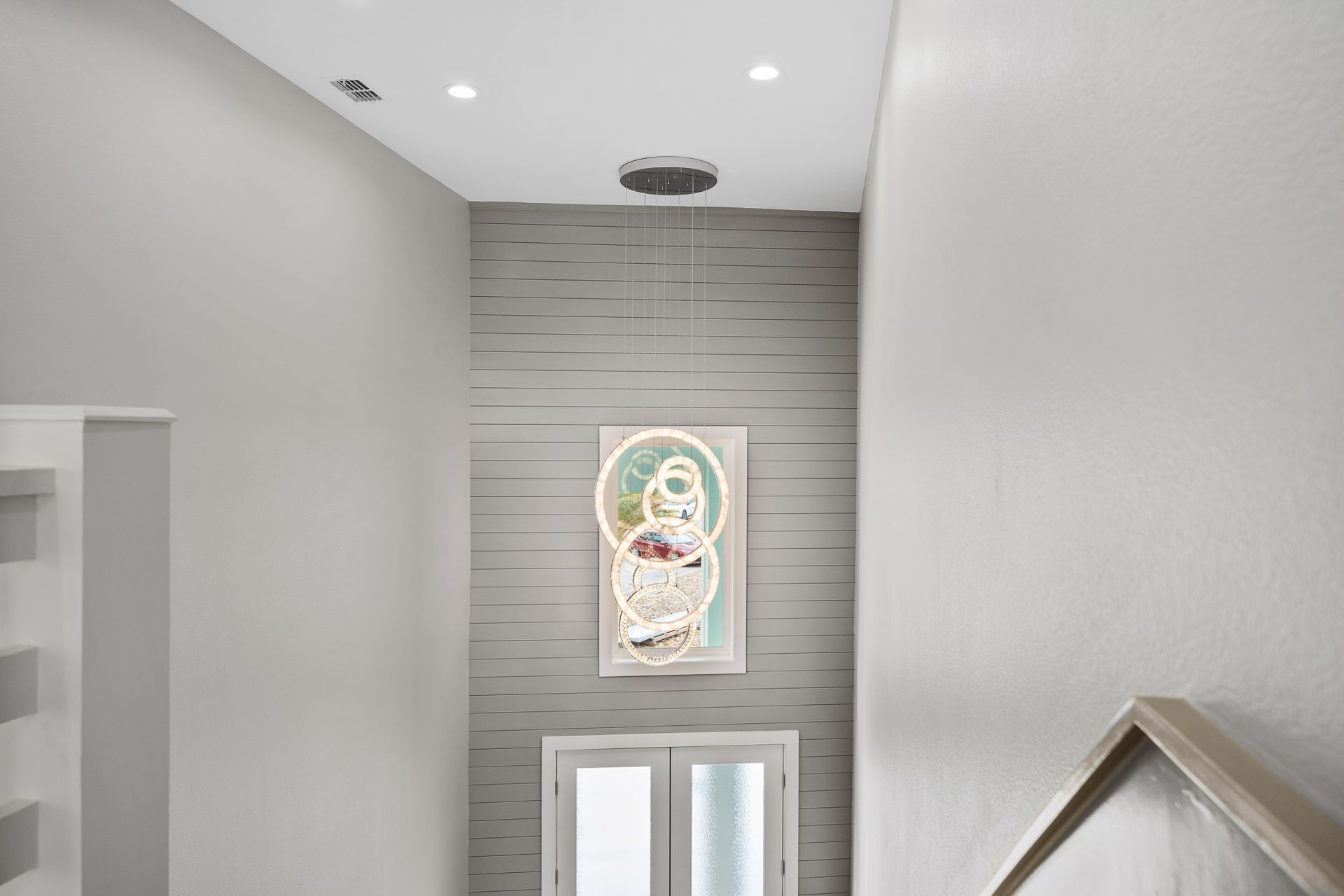 Gray hallway with textured wall, artwork, and a view of a door below. Bright overhead lighting.
