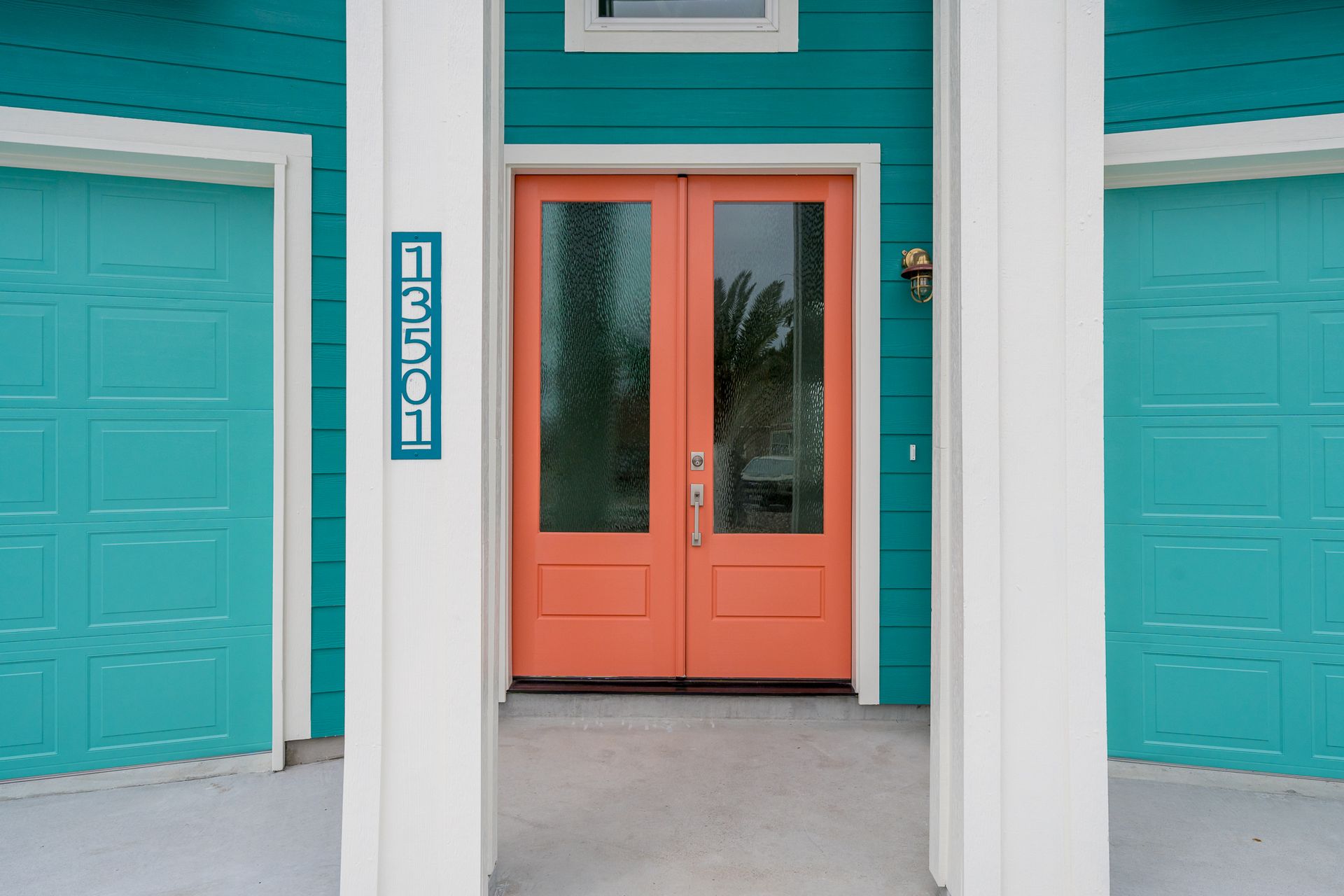 Bright turquoise house with coral door, white columns, and garage doors. House number is on the left.