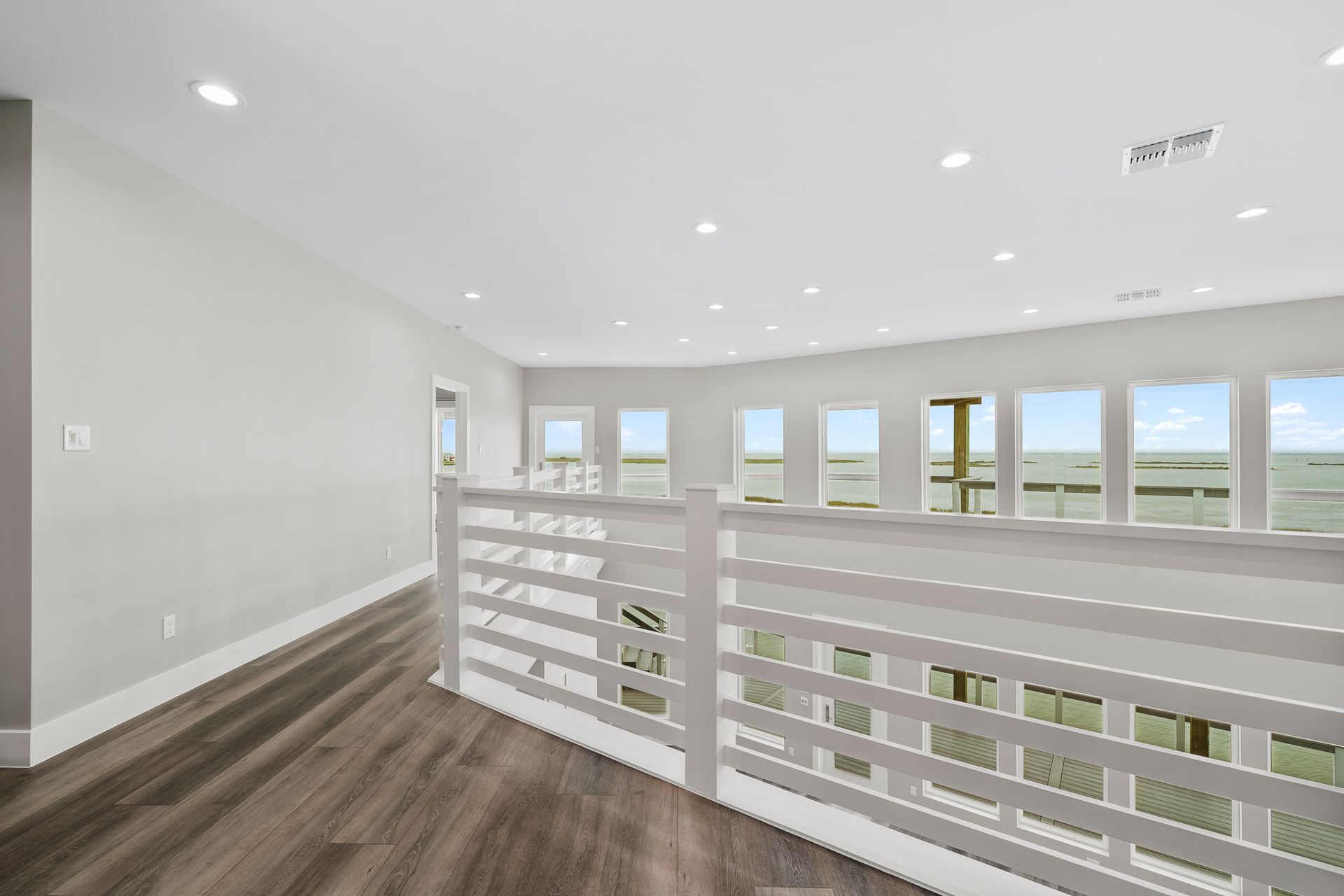 Bright, airy loft with white railing, many windows, and wood flooring.
