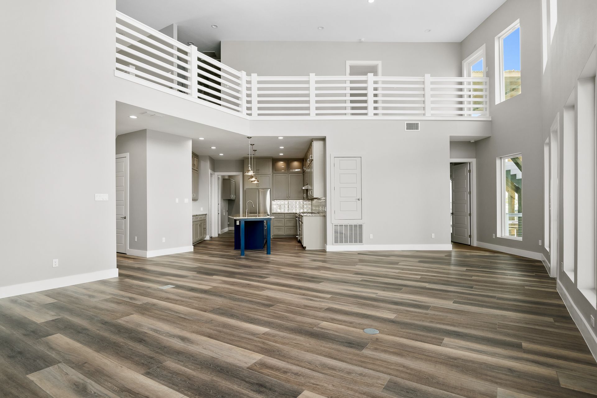 Open-concept living space with kitchen, loft, and large windows, hardwood floors, and gray walls.