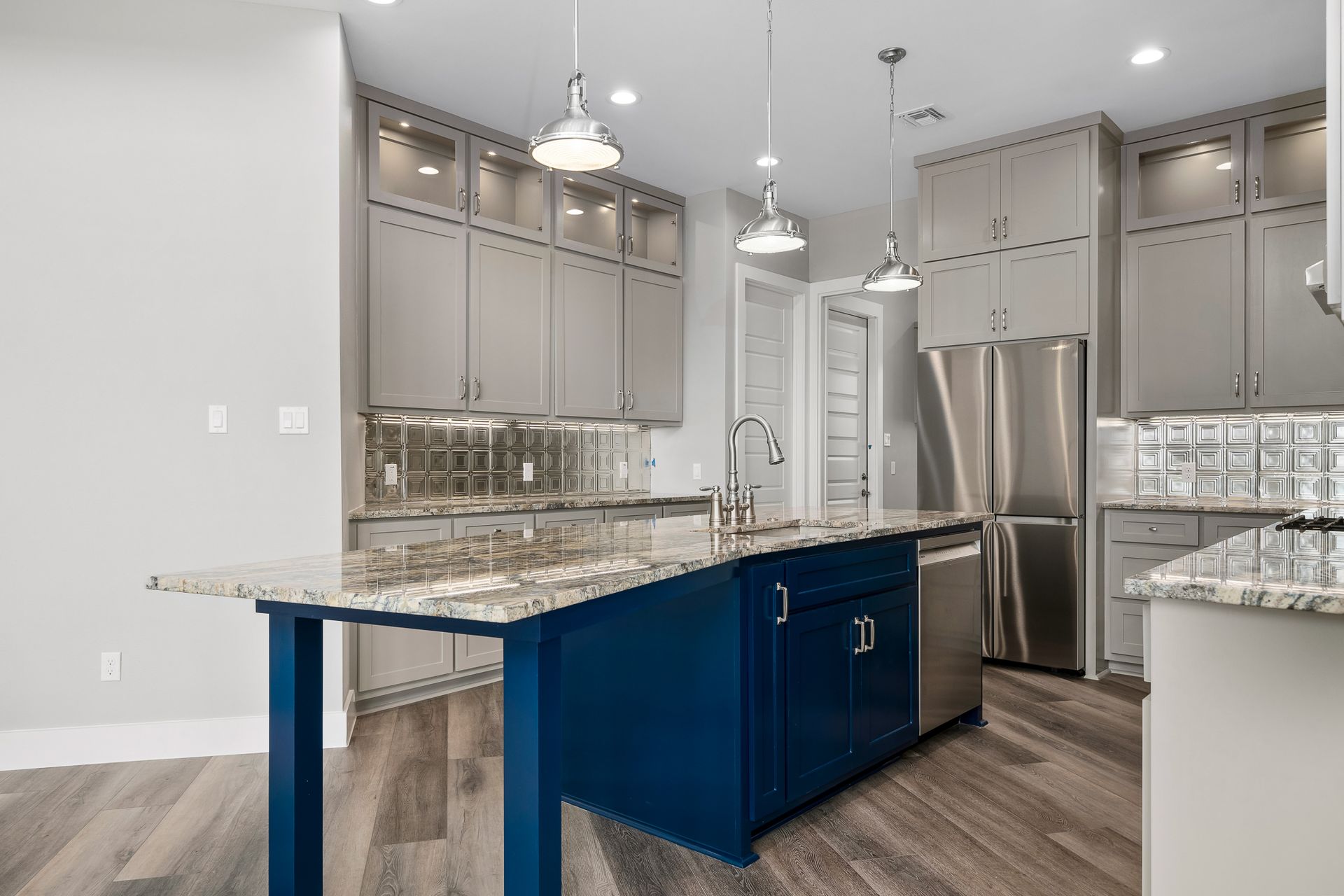 Modern kitchen with blue island, gray cabinets, stainless steel appliances, and granite countertops.