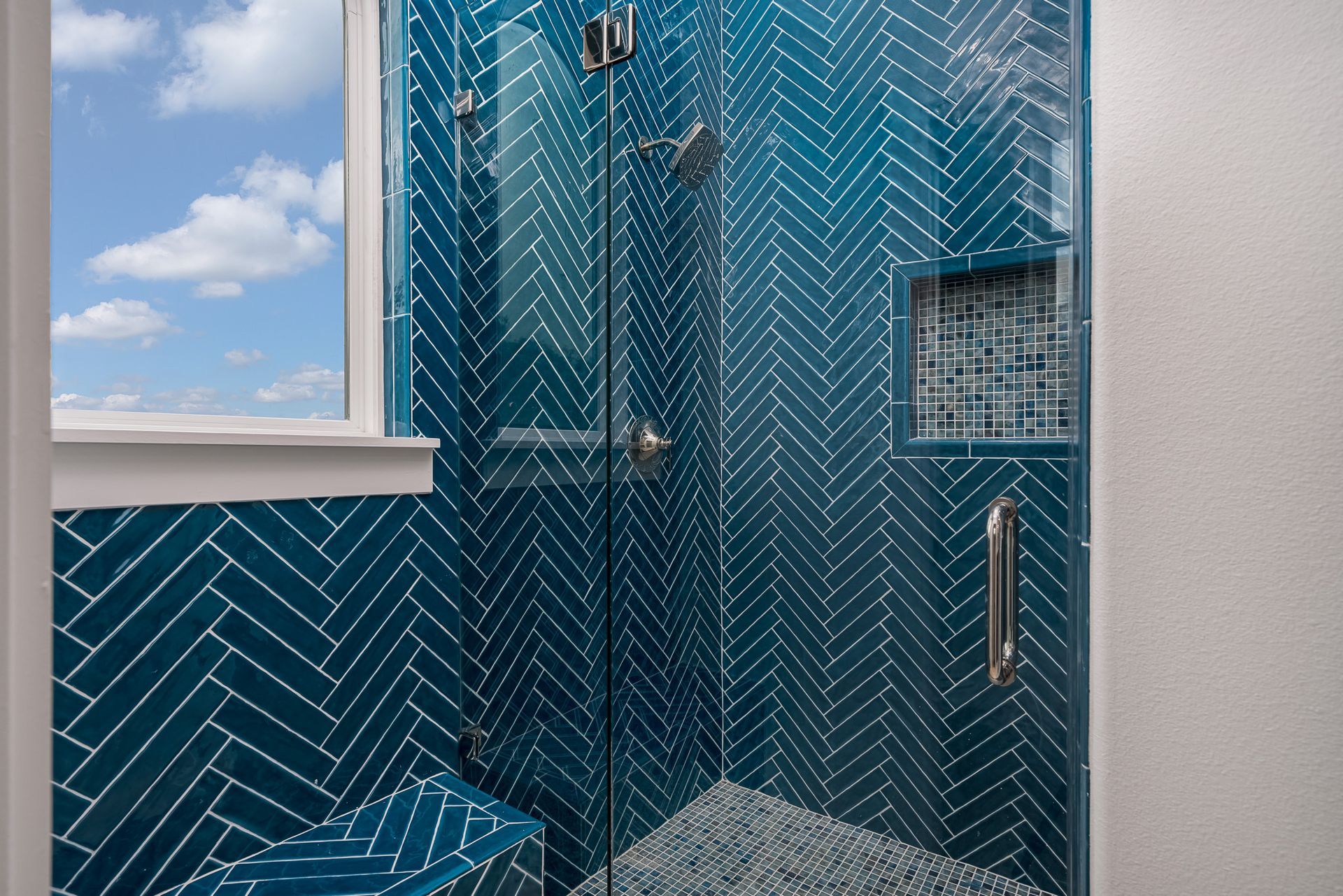 A bathroom with blue tiles and a walk in shower with a glass door.