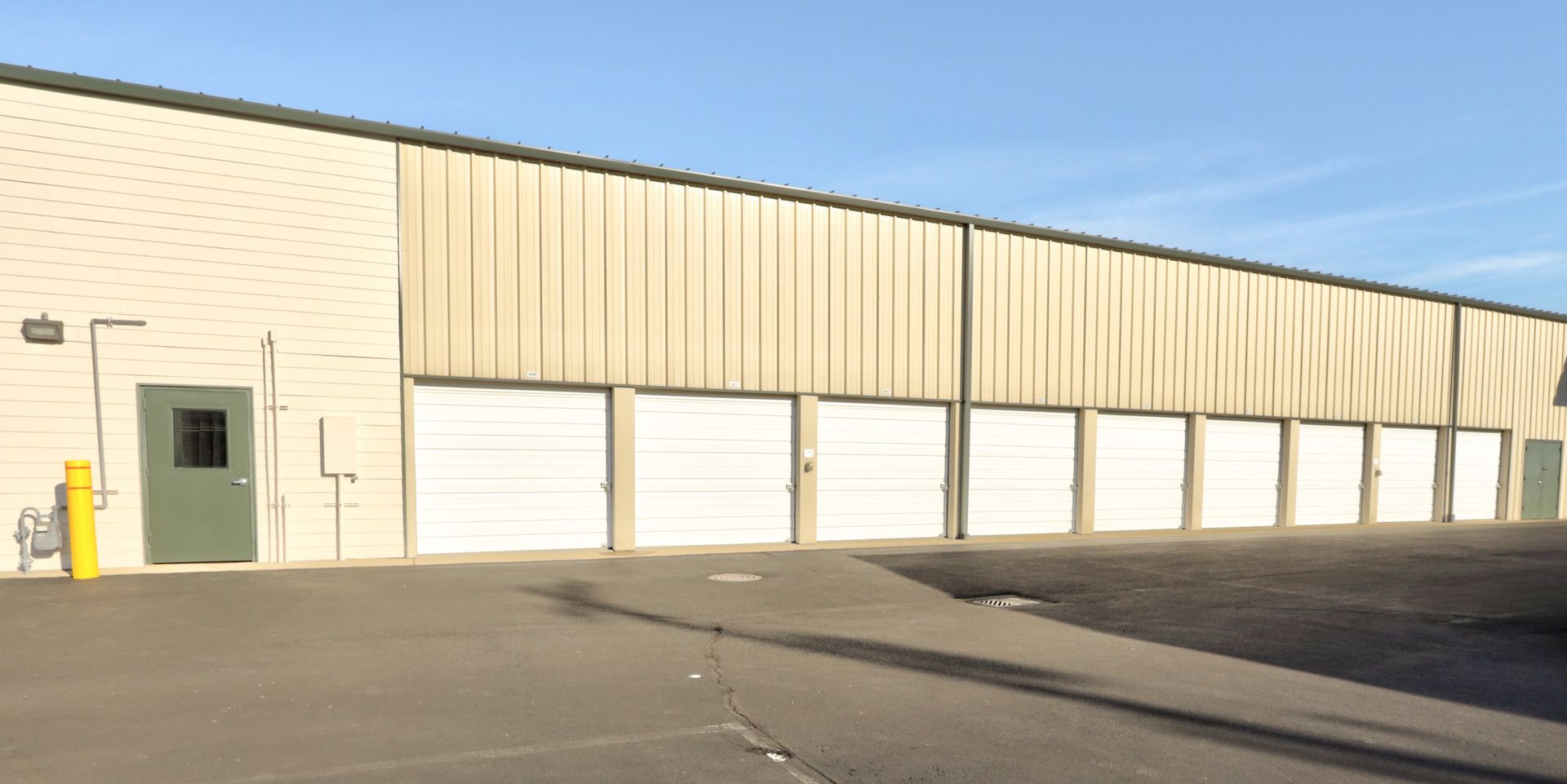 Exterior of storage units with white doors, tan metal siding, and a light blue sky.