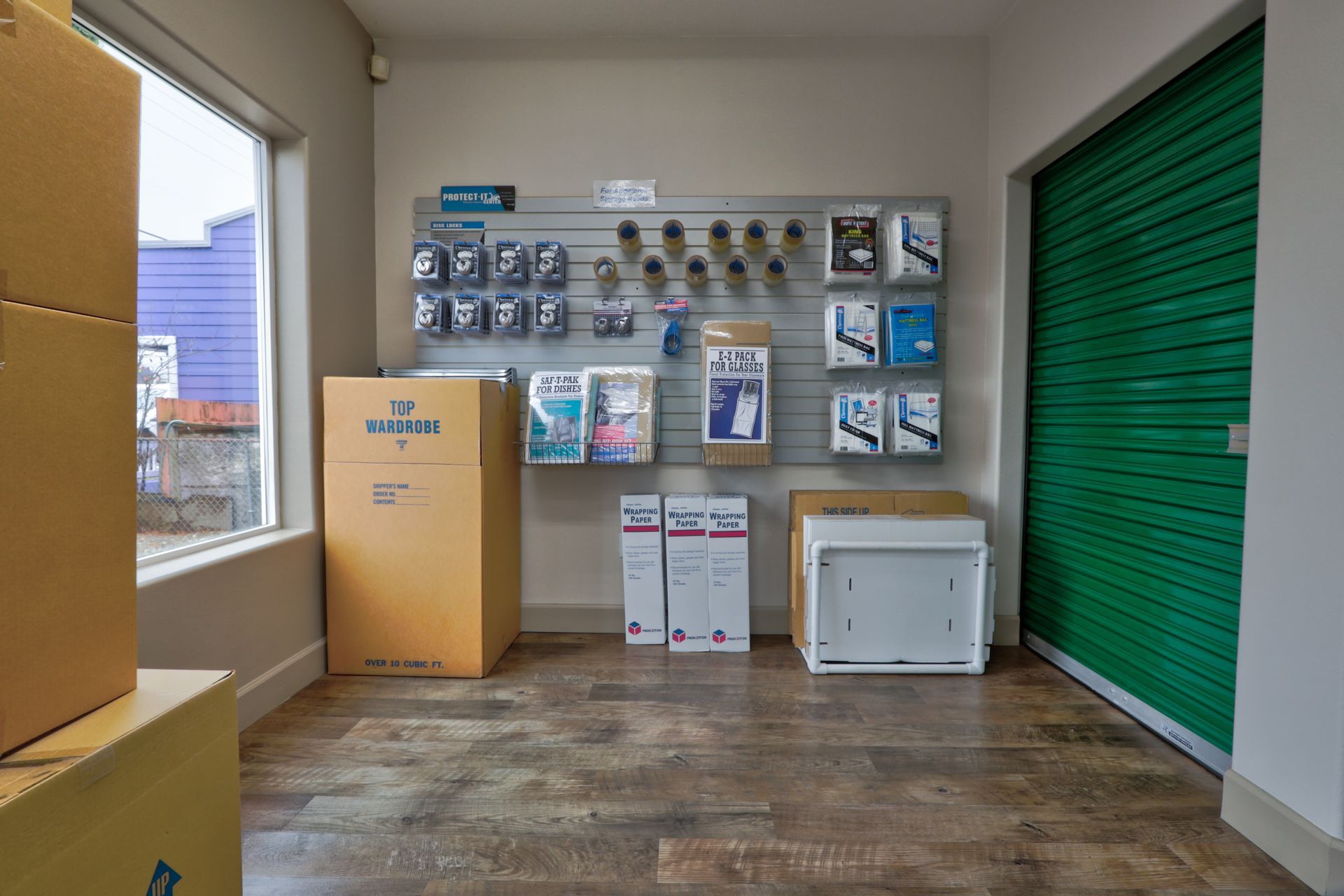 Interior of a storage unit facility, showing boxes, supplies, and green door.