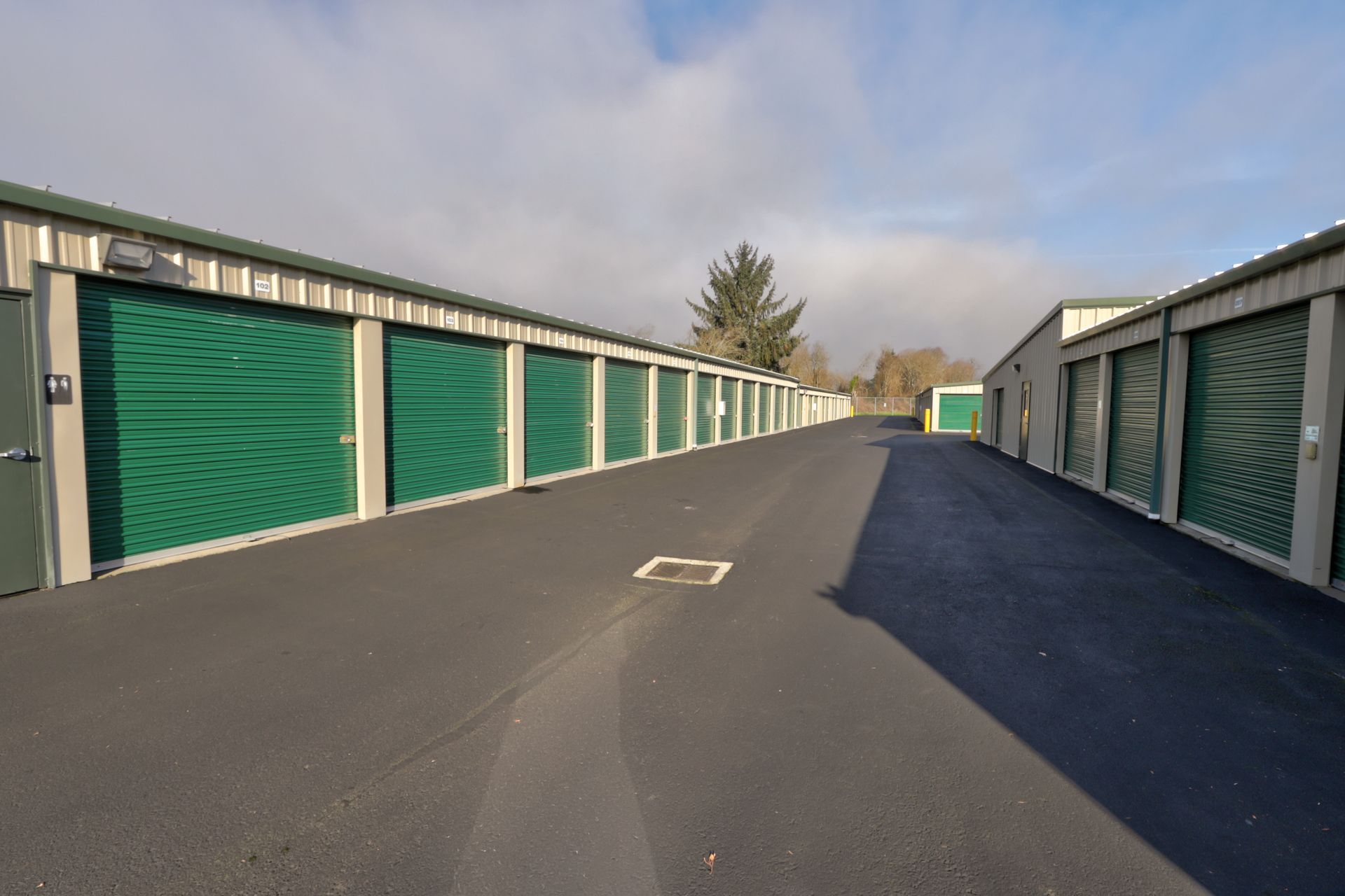 Exterior view of self-storage units with green doors and a paved walkway.