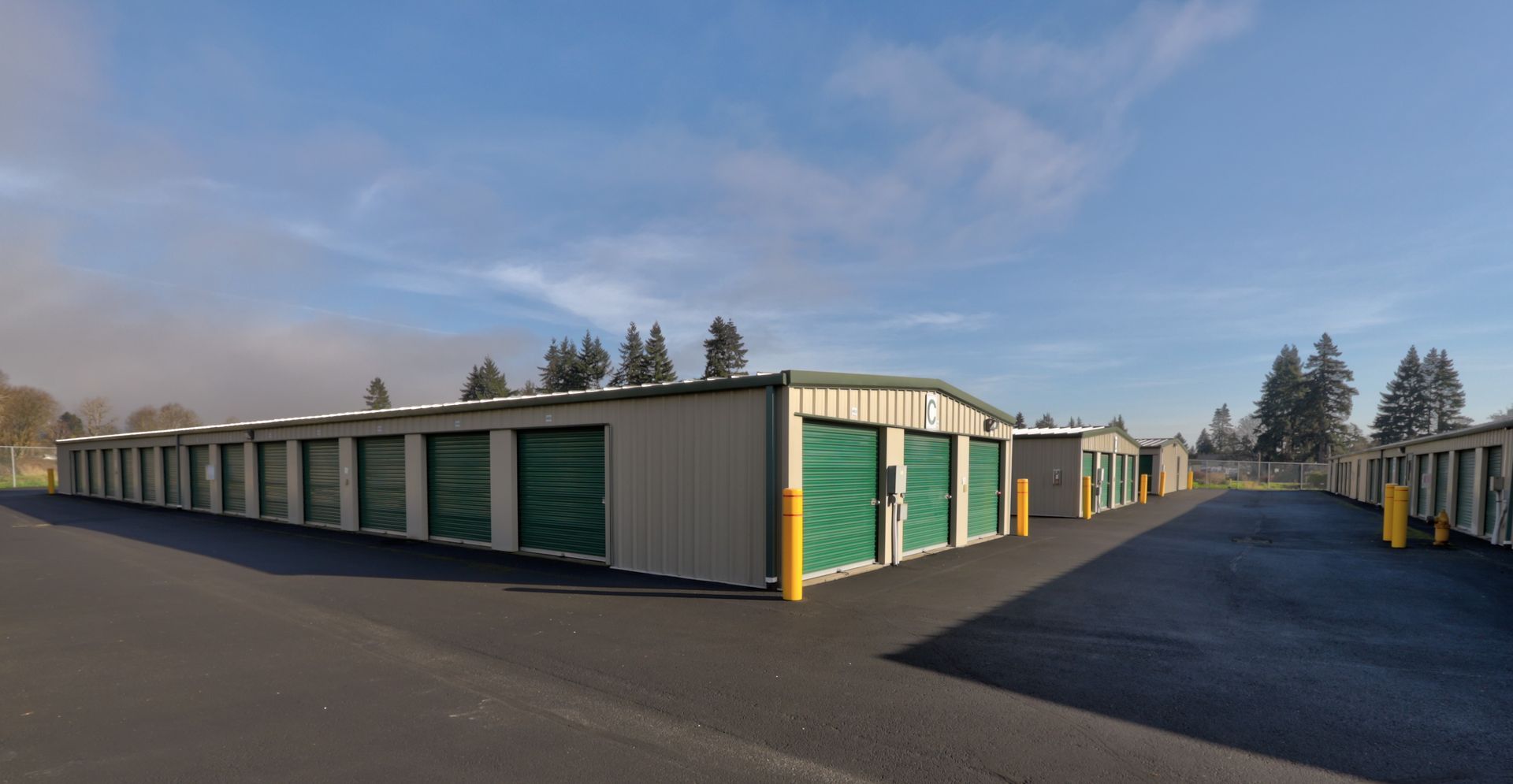 Storage units with green doors and tan walls, set on black asphalt.