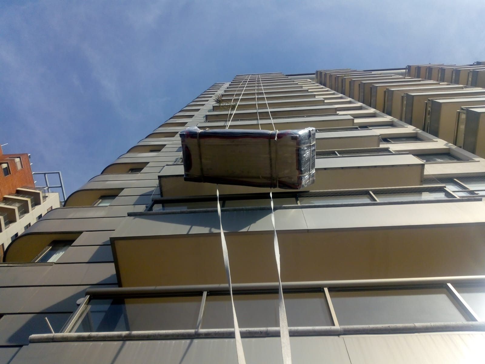 Un objeto envuelto suspendido de un edificio alto y izado mediante correas contra un cielo azul.