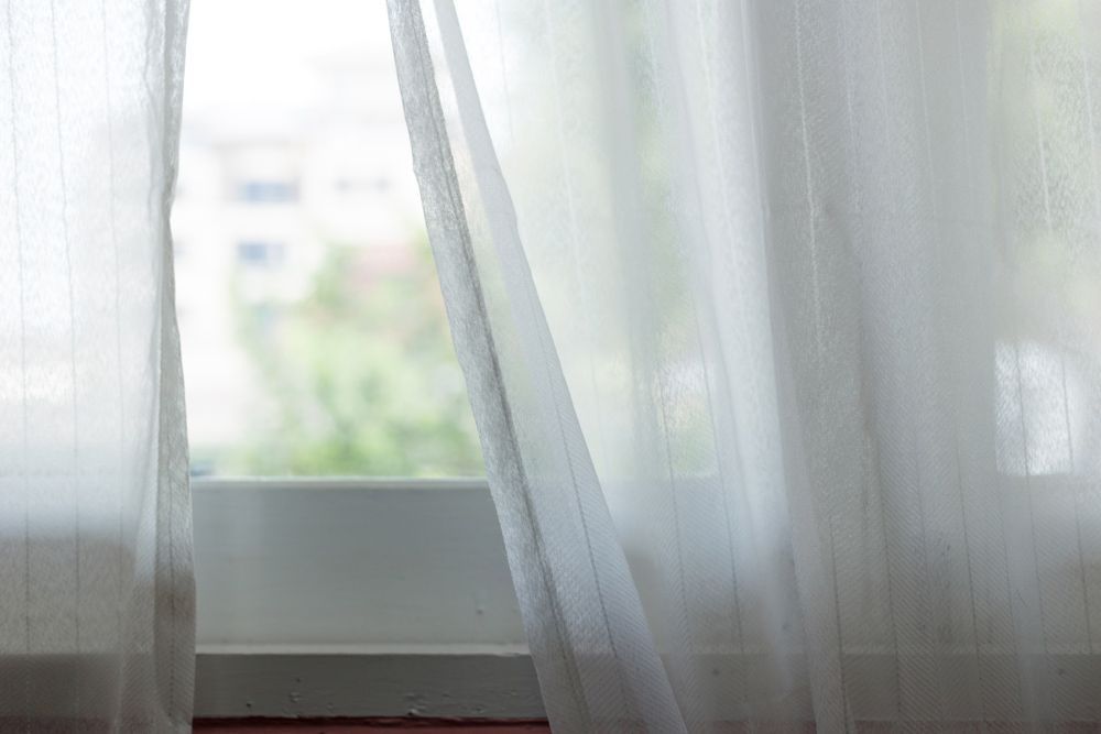 A Close Up of a Window With White Curtains Blowing in the Wind — Artizen Curtains in Coolum, QLD