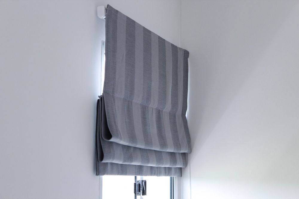 A Gray Striped Roman Shade is Hanging on a Window — Artizen Curtains in Coolum, QLD