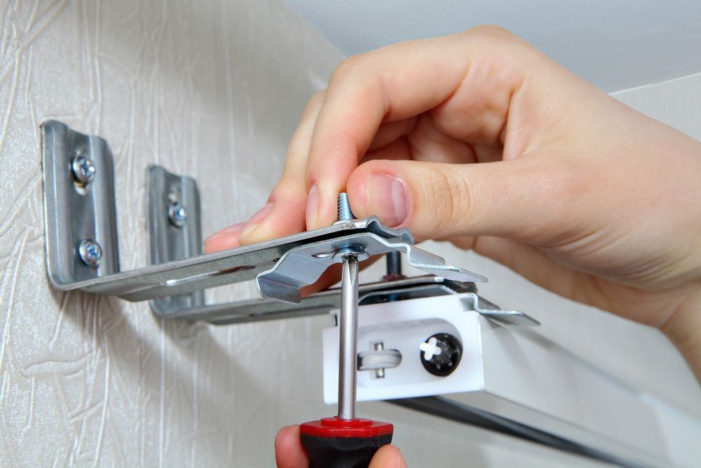 A Person is Installing a Blind on a Wall With a Screwdriver — Artizen Curtains in Mooloolaba, QLD