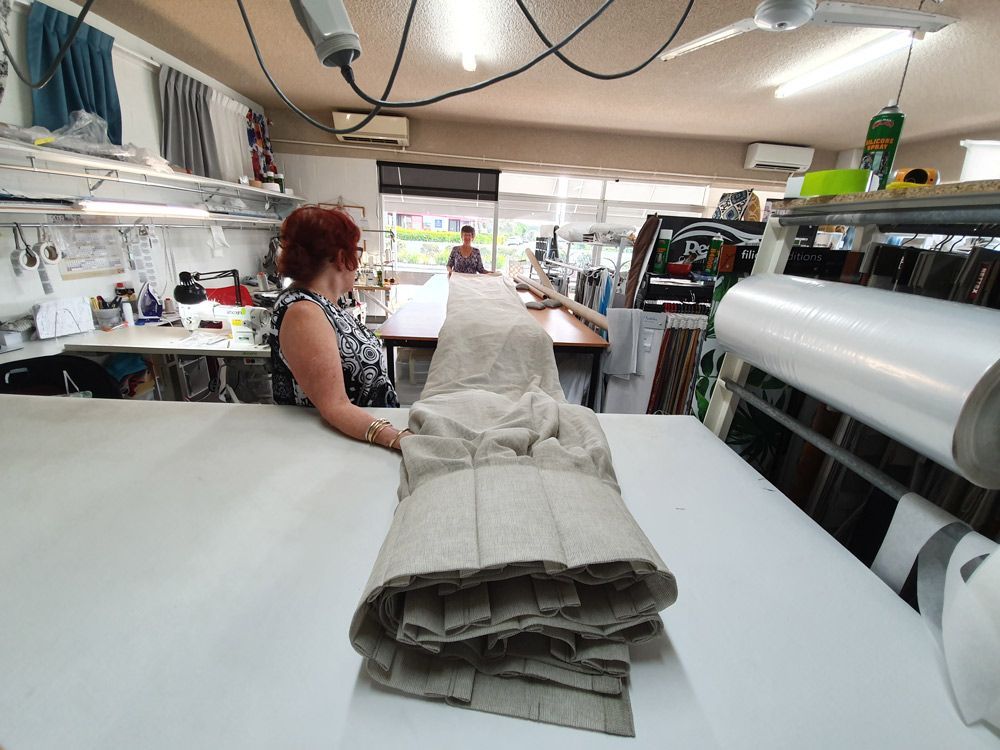 A Woman Is Sitting at A Table in A Factory Looking at A Piece of Fabric — Artizen Curtains in Mooloolaba, QLD