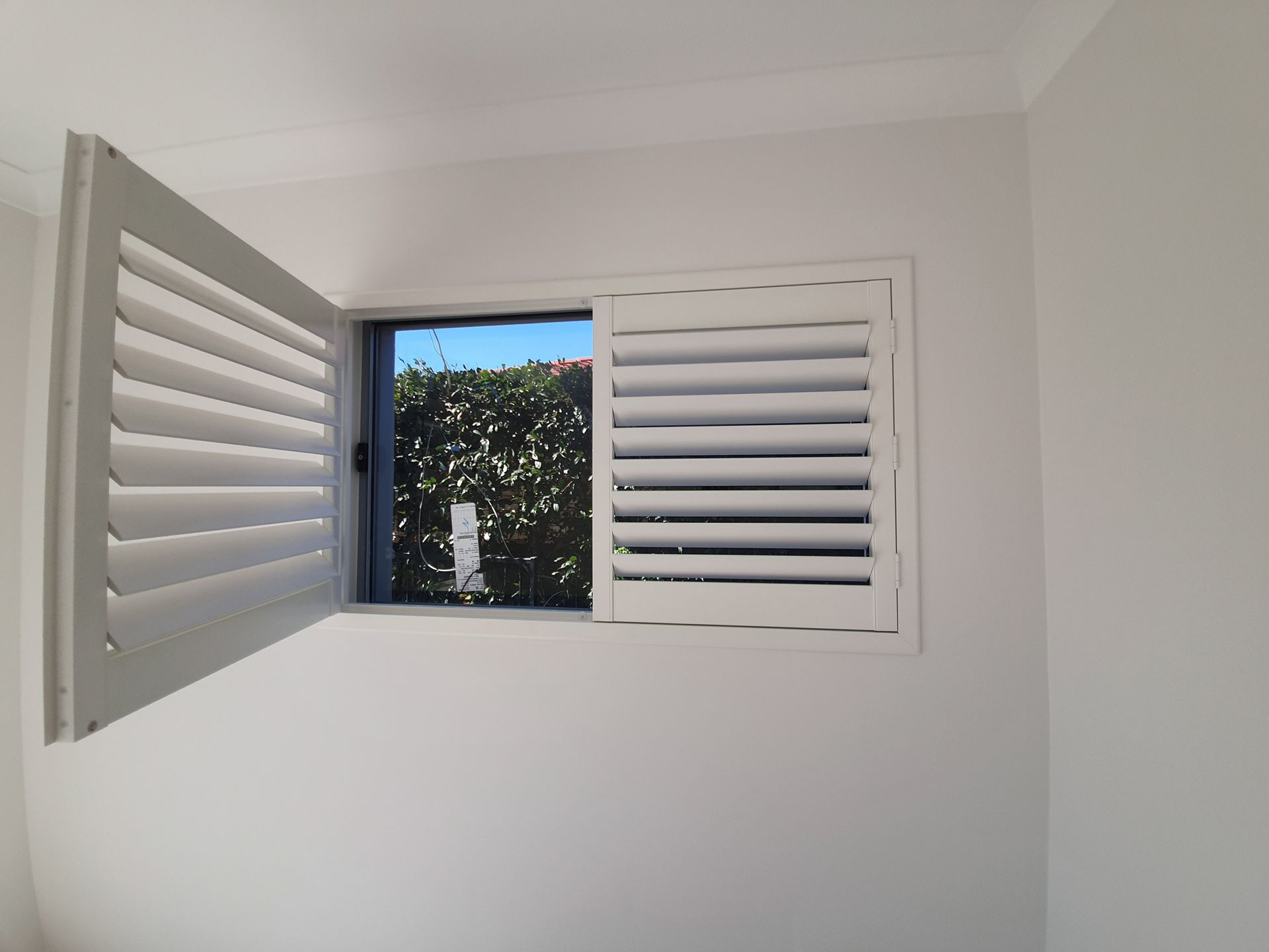 A Window With White Shutters is Open in a Room — Artizen Curtains in Mooloolaba, QLD