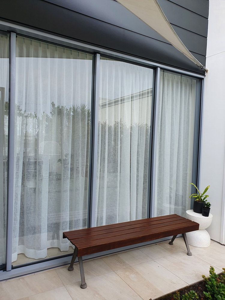 A Wooden Bench Is Sitting in Front of A Large Window — Artizen Curtains in Maroochydore, QLD