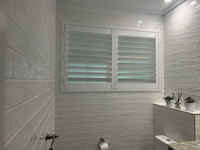 A Bathroom With White Tiles, a Toilet, and a Window With Shutters — Artizen Curtains in Mooloolaba, QLD