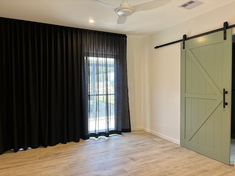 A Bedroom With a Sliding Barn Door and Black Curtains — Artizen Curtains in Mooloolaba, QLD