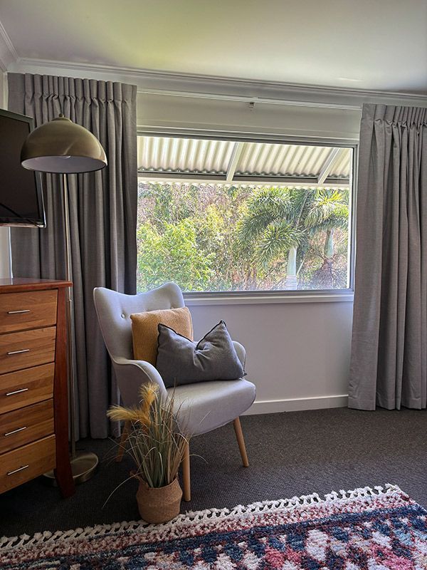 A Living Room With a Chair, Dresser, Lamp and Window — Artizen Curtains in Mooloolaba, QLD