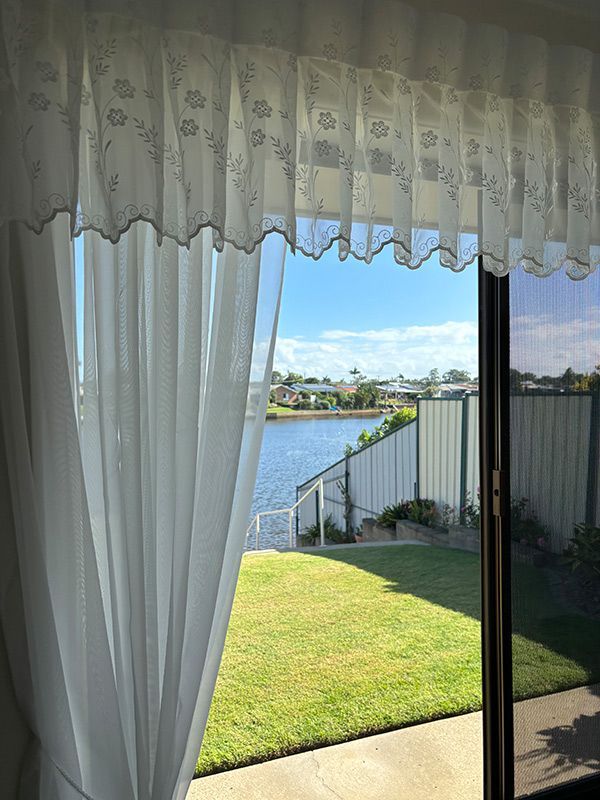 A View of a Lake Through a Sliding Glass Door With White Curtains — Artizen Curtains in Mooloolaba, QLD