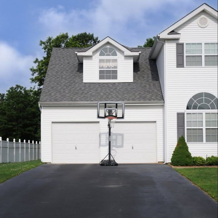 White house with basketball hoop in driveway. Blue sky.