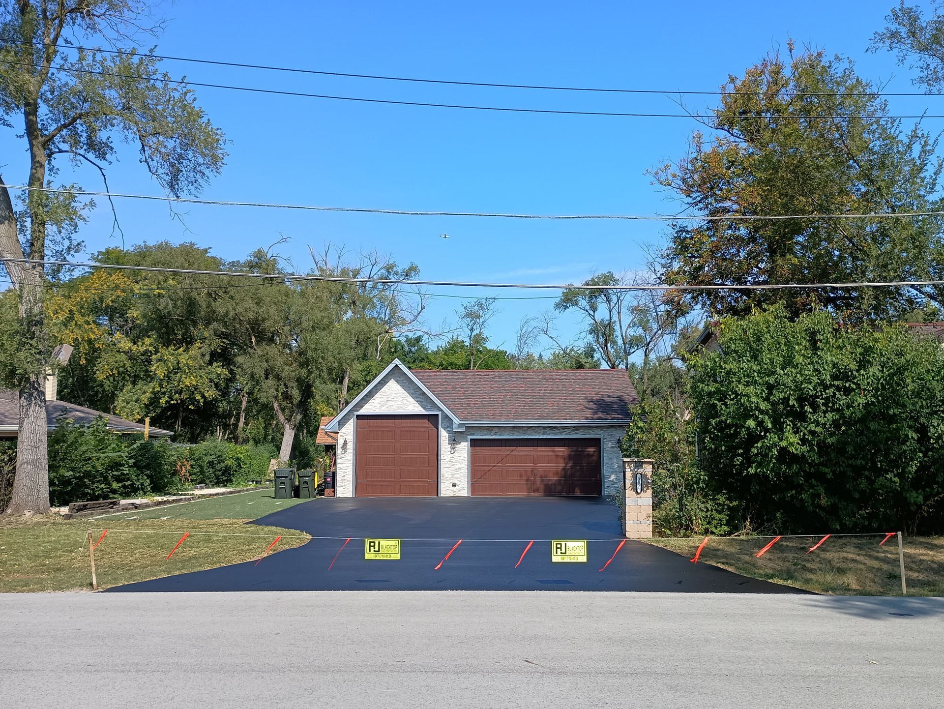 Black paved driveway leads to a two-car garage with brown doors, under a clear blue sky.
