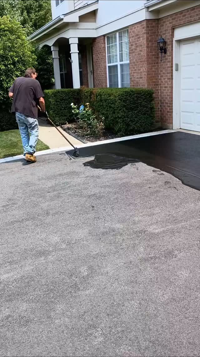 Man applying sealant to a driveway in front of a brick house.