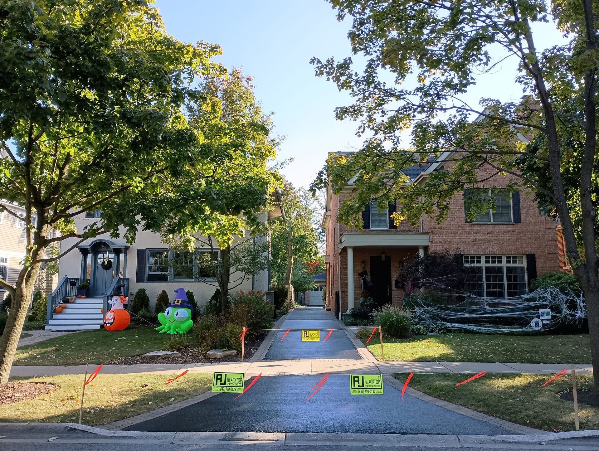 Two houses with driveways blocked by construction. Halloween decorations on the lawns.