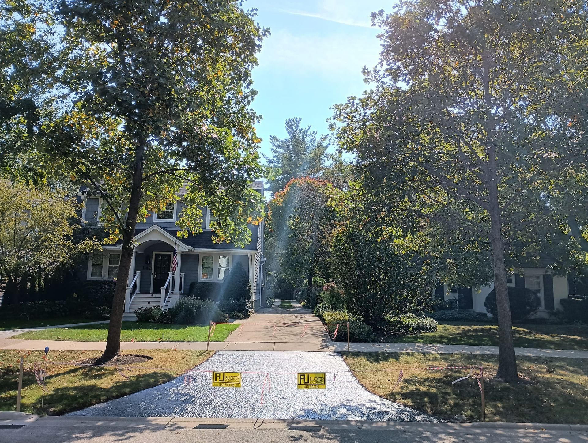 Gravel driveway with caution signs. Trees frame a two-story house on a sunny day.