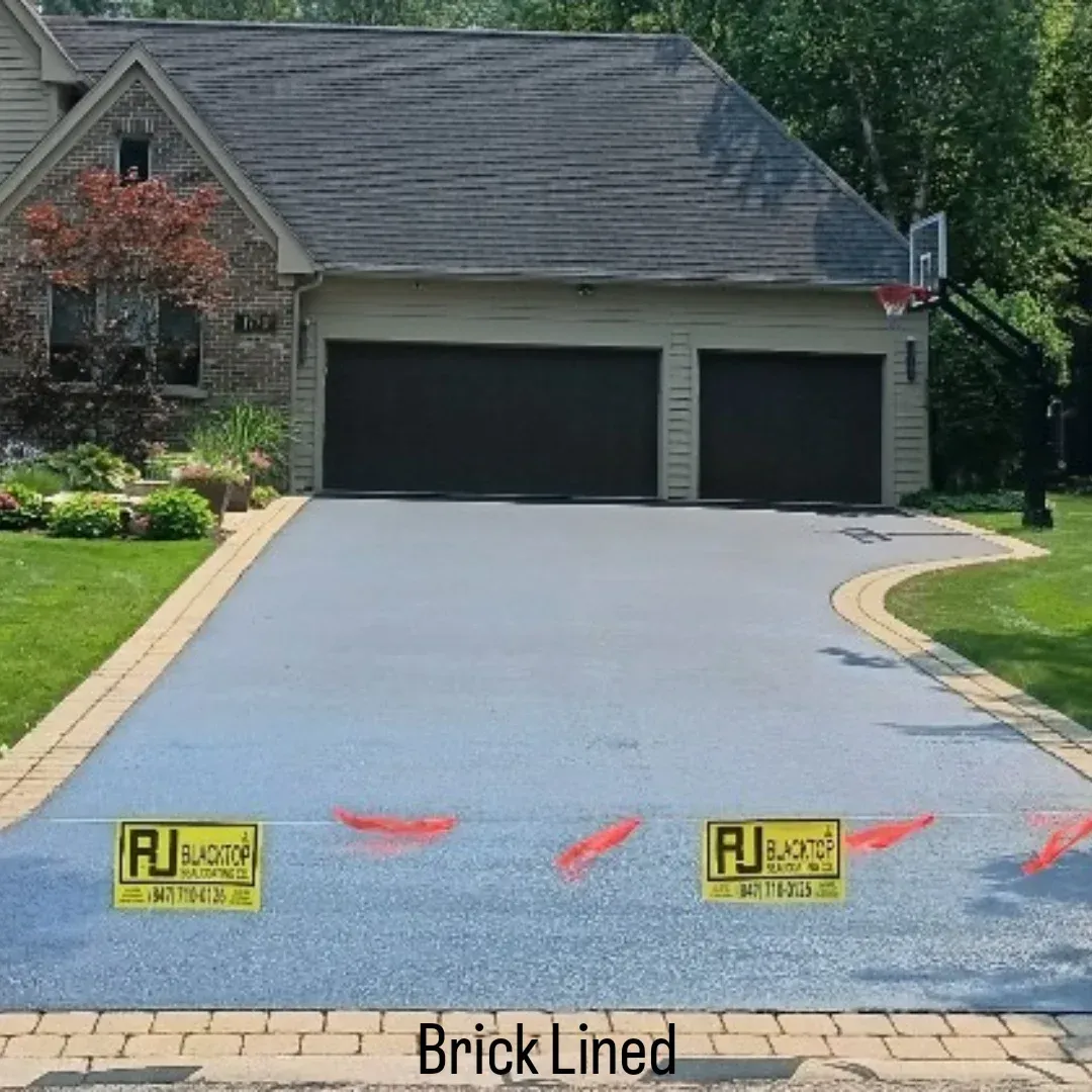 House with a resurfaced blue driveway, brick-lined edges, and black garage doors; basketball hoop.