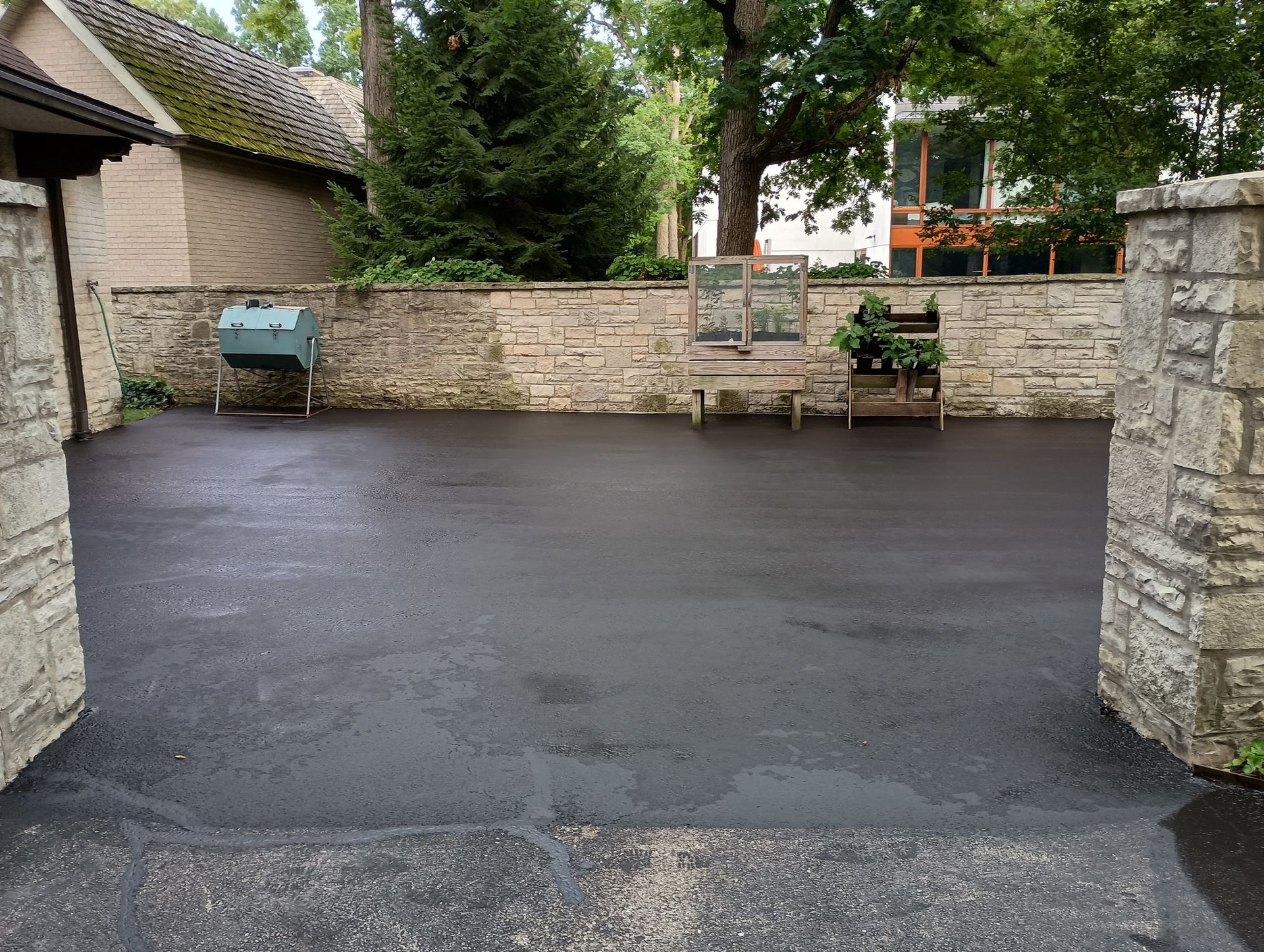 Paved courtyard bordered by stone walls, gate, and structures, with greenery and sky visible.
