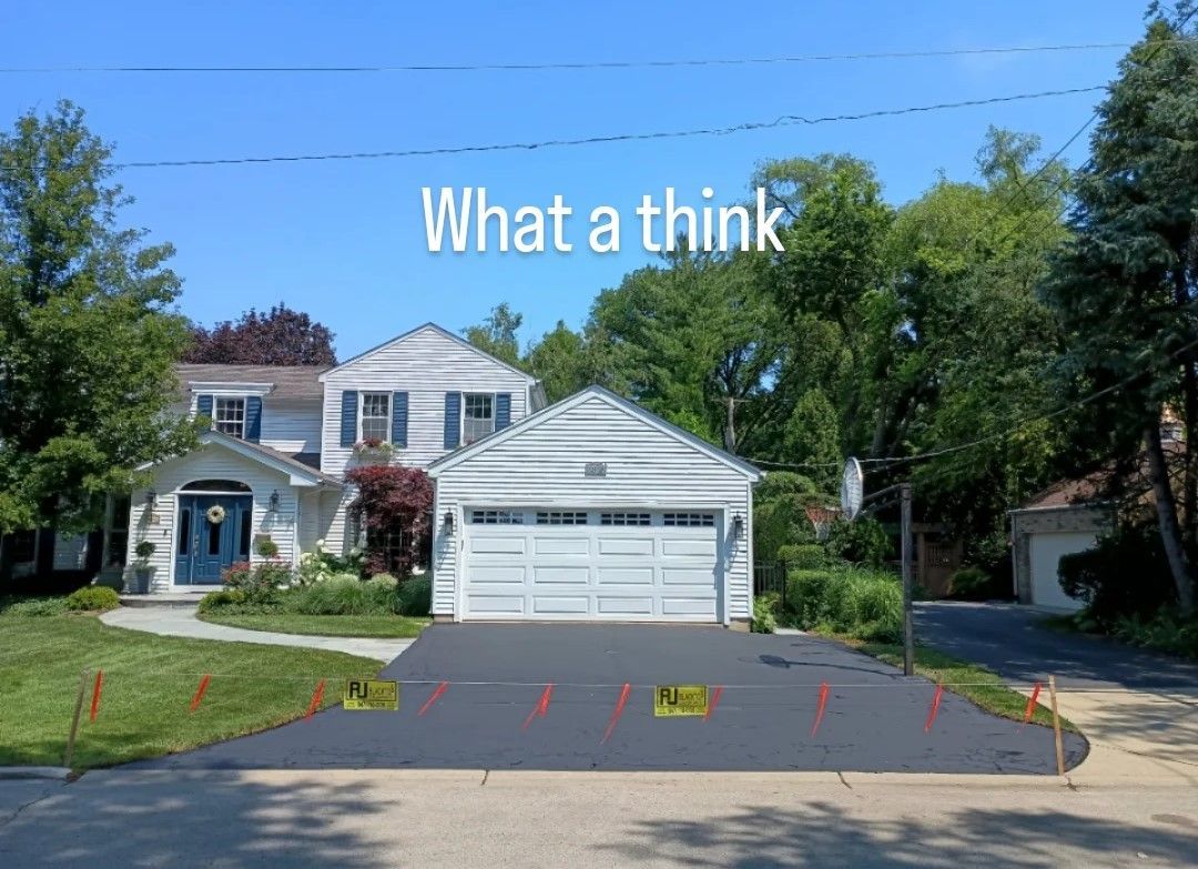 A newly paved asphalt driveway in front of a two-story house with a white garage, under a blue sky.