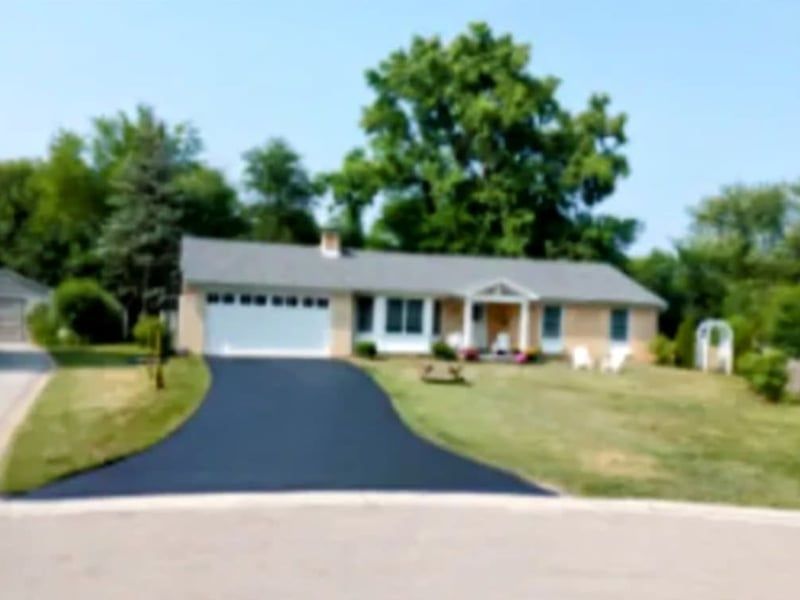 A ranch-style house with a black driveway and green lawn, under a clear blue sky.