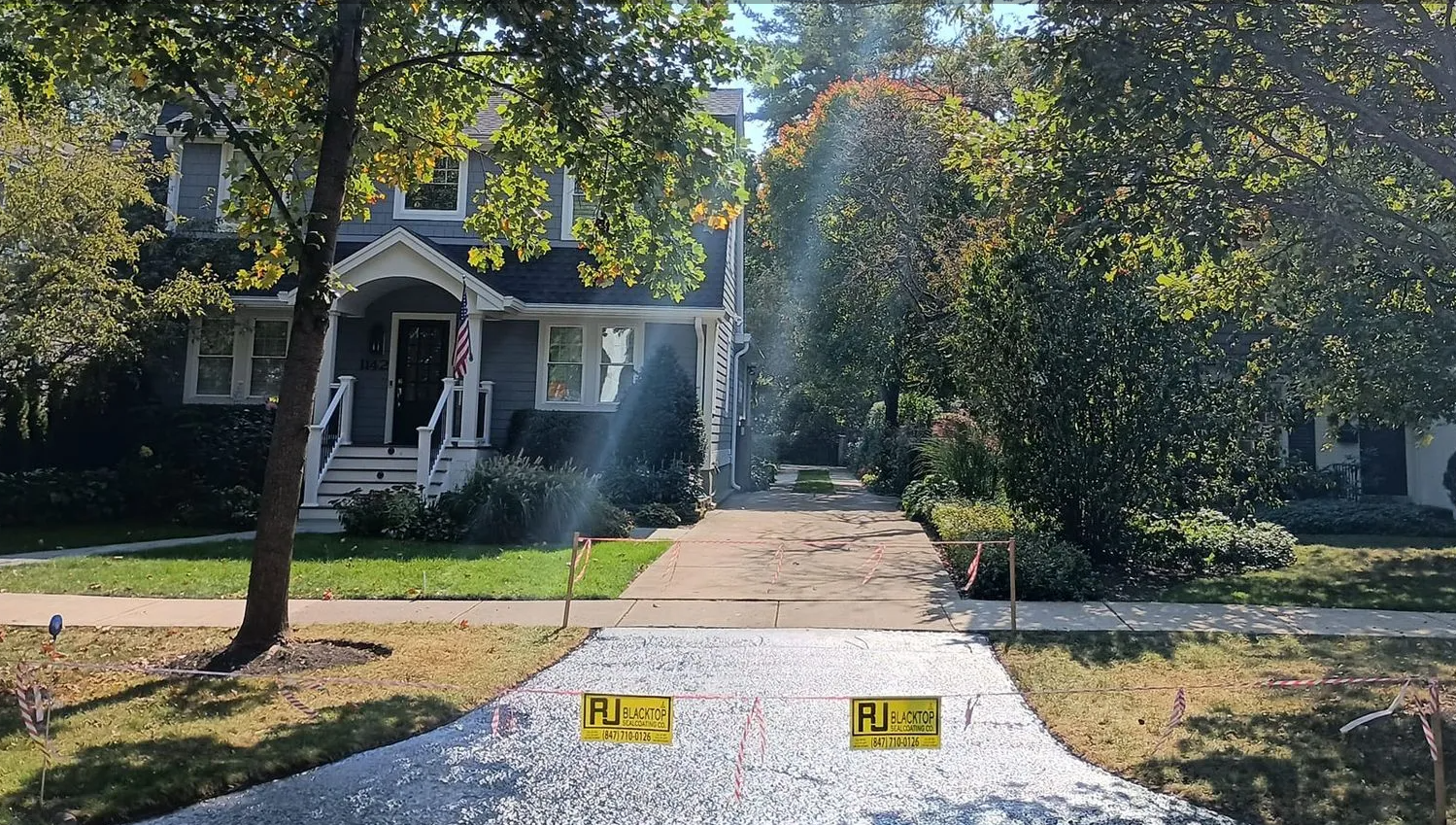 Gravel driveway with caution signs. Trees frame a two-story house on a sunny day.