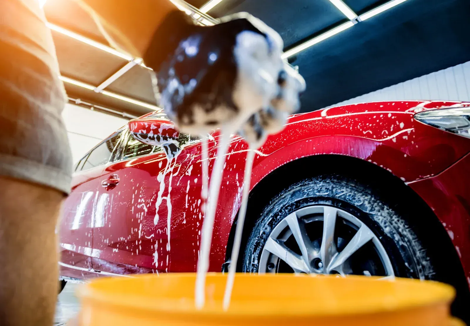 Person washing a red car with soapy water at a car wash.