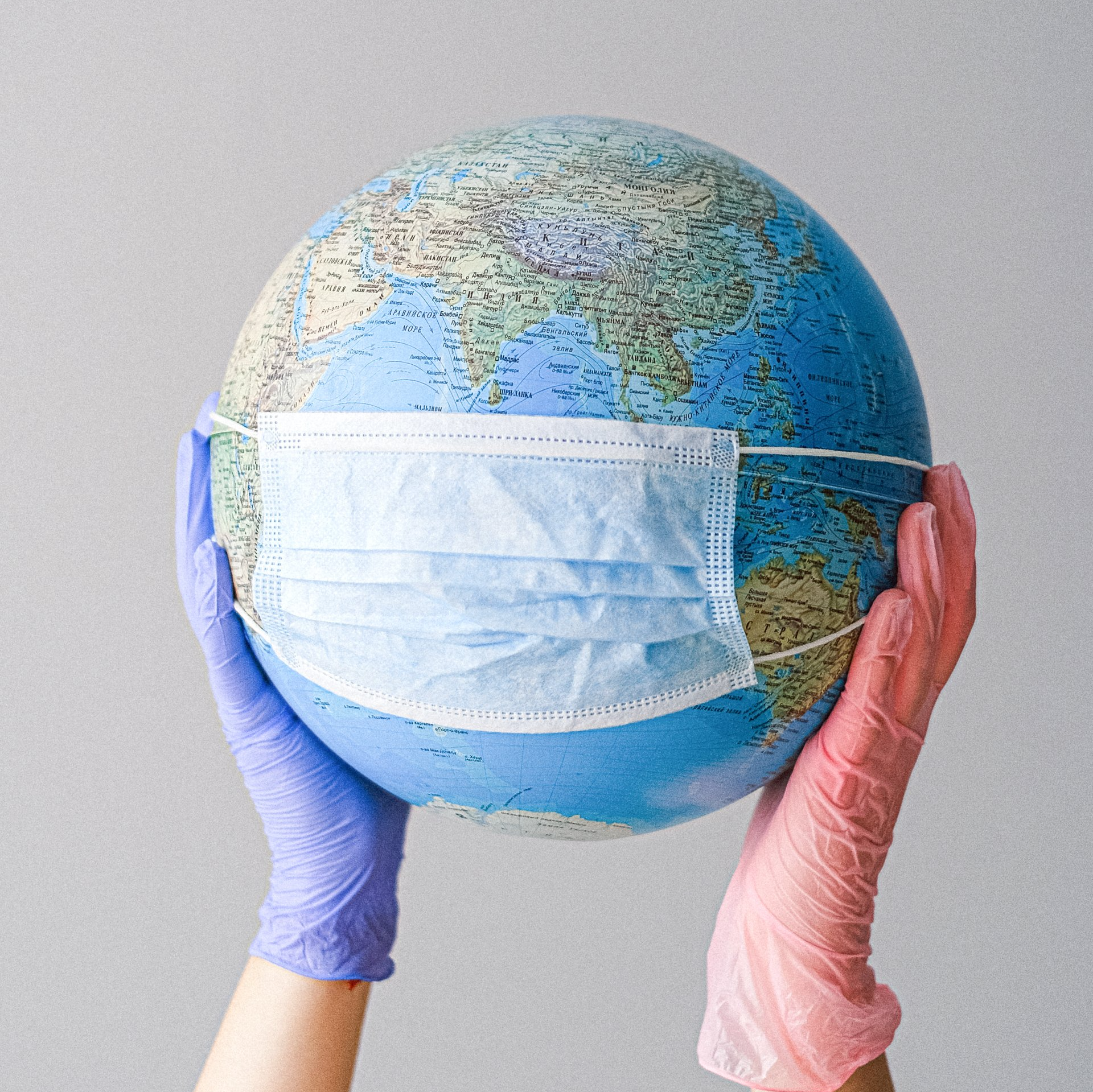 A person wearing gloves is holding a globe with a mask on it.