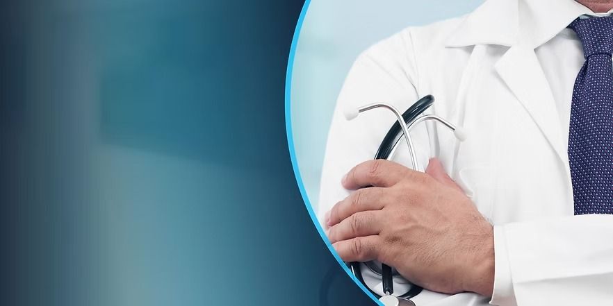 Un médico con bata blanca sostiene un estetoscopio con los brazos cruzados. Fondo azul.