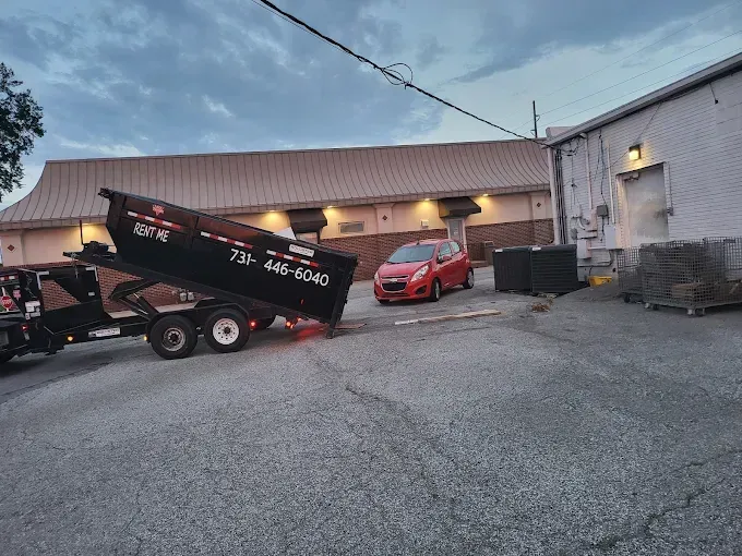 Orange dumpster filled with construction debris, parked outside with trees in the background.