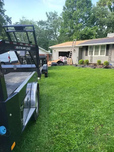 A trailer parked on a lawn next to a house with workers on the roof.