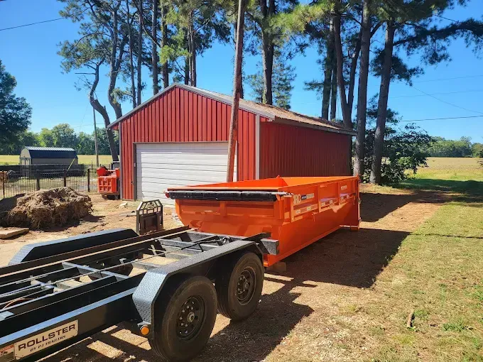 Orange dumpster on a trailer in front of a red shed.