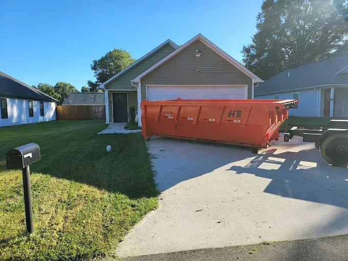 Orange dumpster on a residential driveway in front of a house.